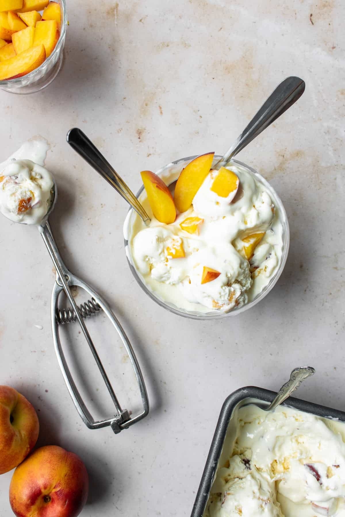 Peach ice cream in a bowl and in a scoop on a surface with whole peaches.