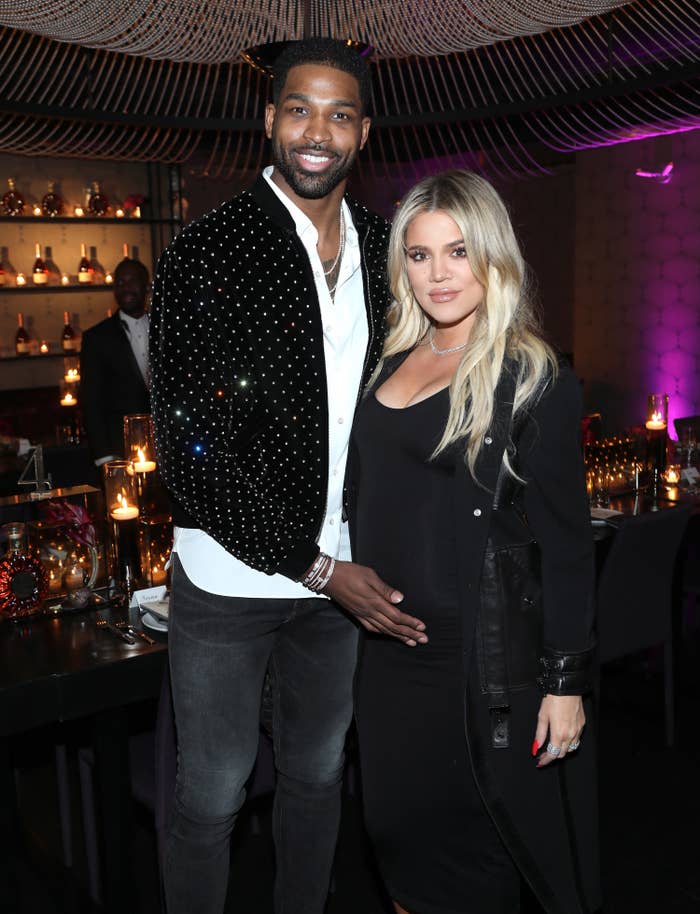 Thompson, in a sparkly jacket and black jeans, puts his hand on Khloe&#x27;s belly at an event