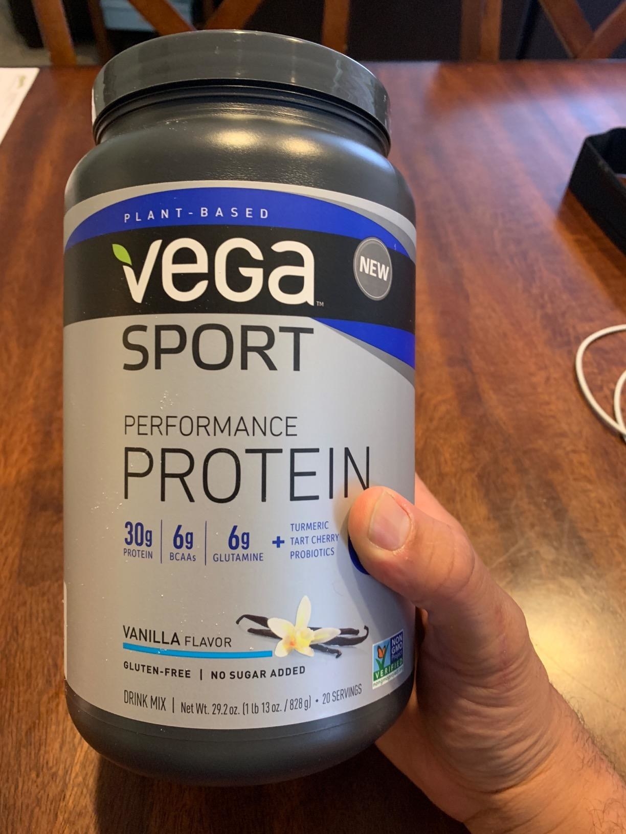 a reviewer hand holding a jar of the protein powder