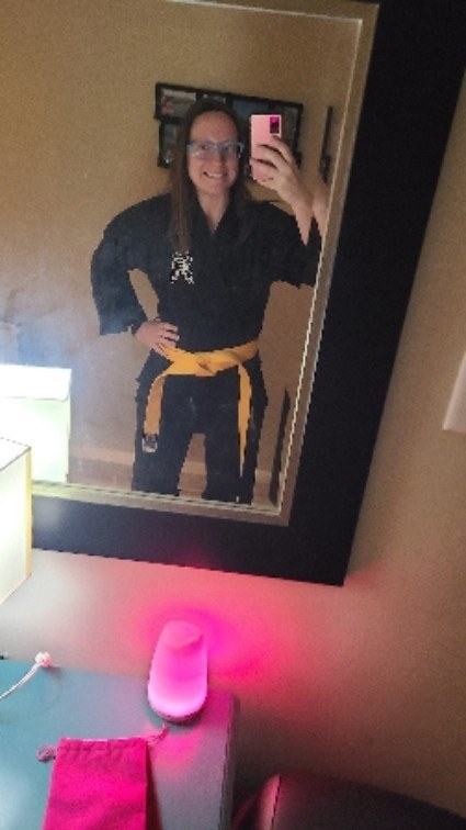 Woman with beginner yellow belt poses with a smile in front of her mirror
