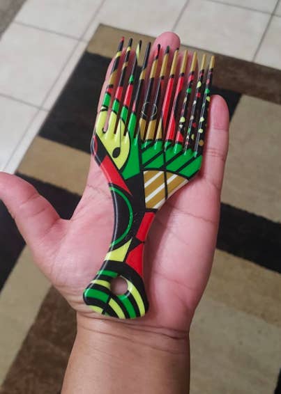 reviewer&#x27;s hand with a thick plastic afro pick featuring a vibrant red, black, green, and yellow print