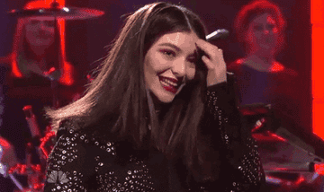 GIF of Lorde smiling and placing her hair behind her ear
