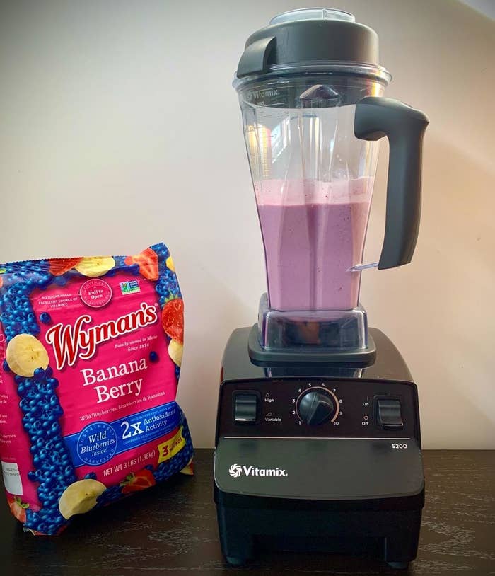 a reviewer photo of the blender filled with a purple liquid witting next to a bag of frozen fruits.