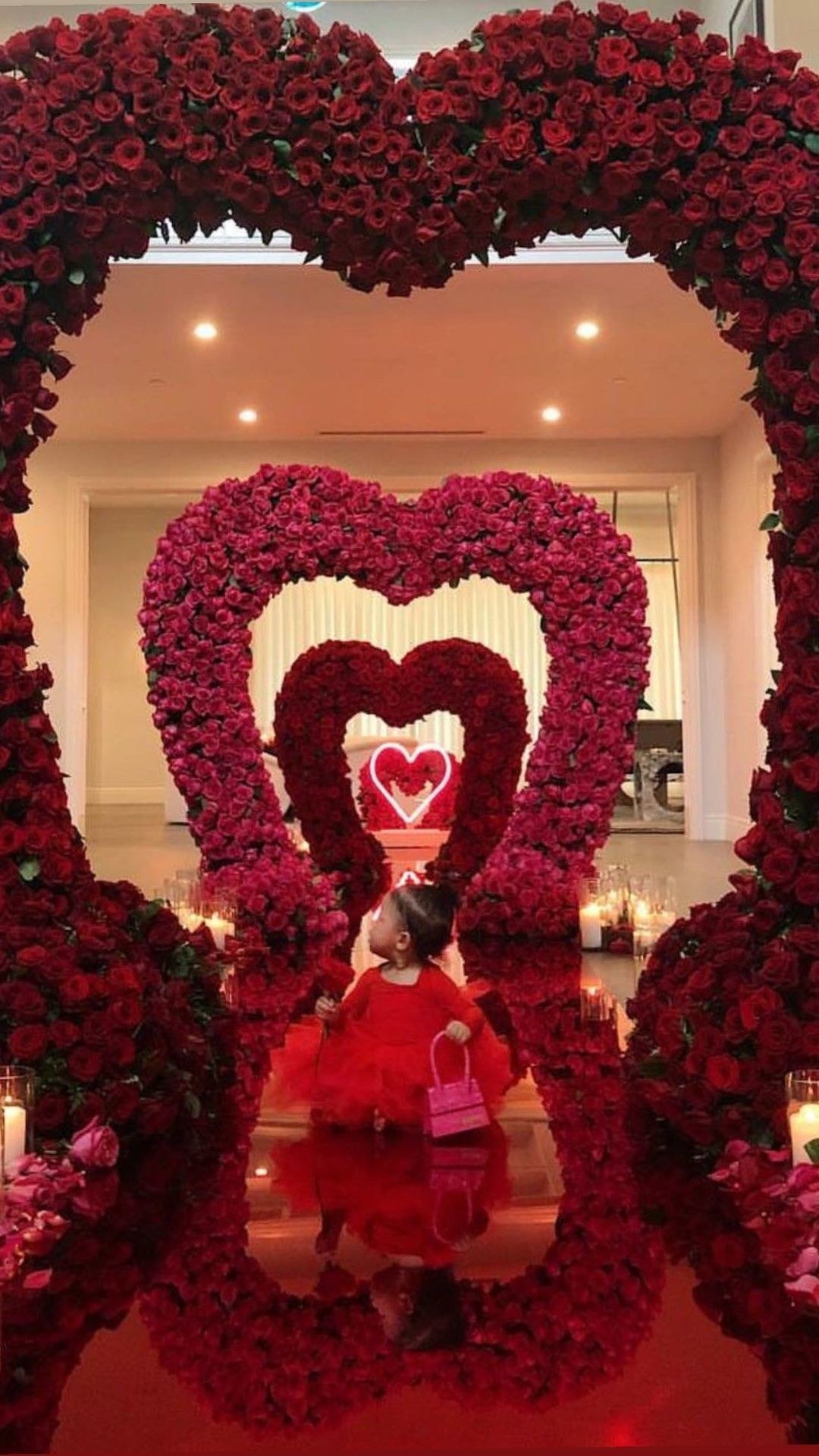 Stormi standing under one of multiple hearts shaped out of roses