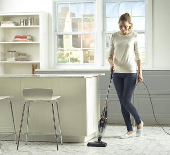 Model using stick vacuum on floor