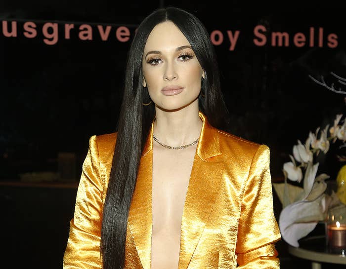 Kacey wears a shiny yellow blazer with no shirt underneath