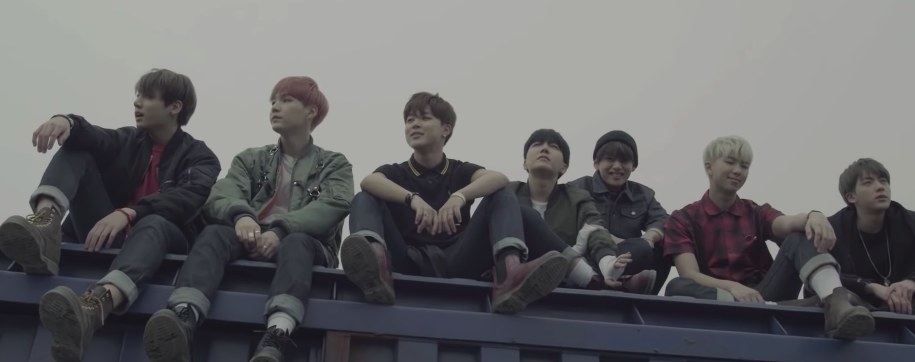 BTS sit in a row on top of a train car in the I Need U music video