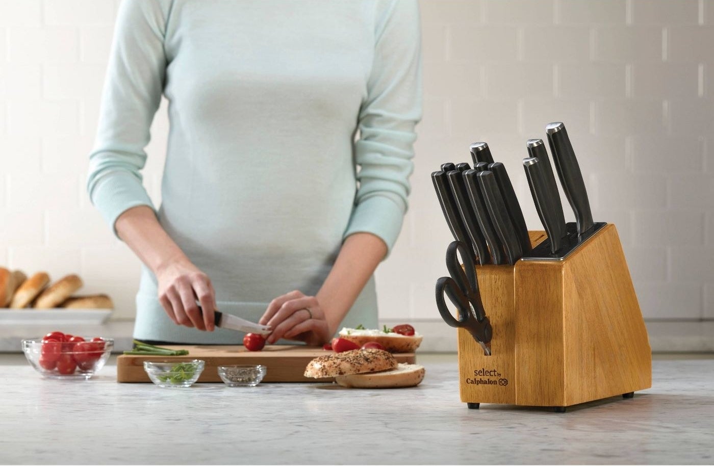 calphalon knife set in a wood block on a table next to a model cutting vegetables
