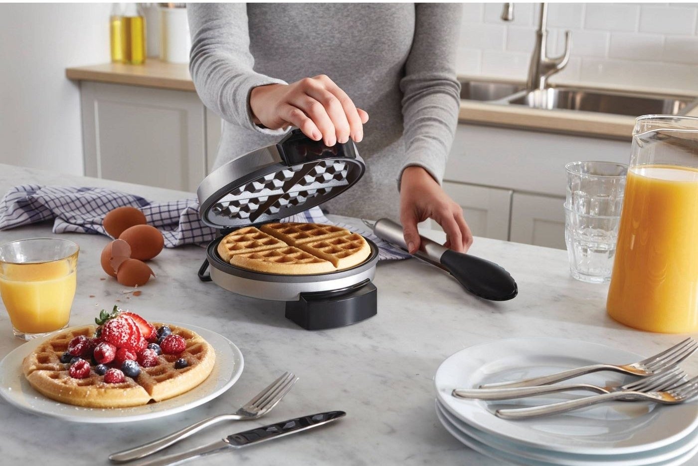 model holding silver waffle maker with waffle inside next to a waffle on a plate