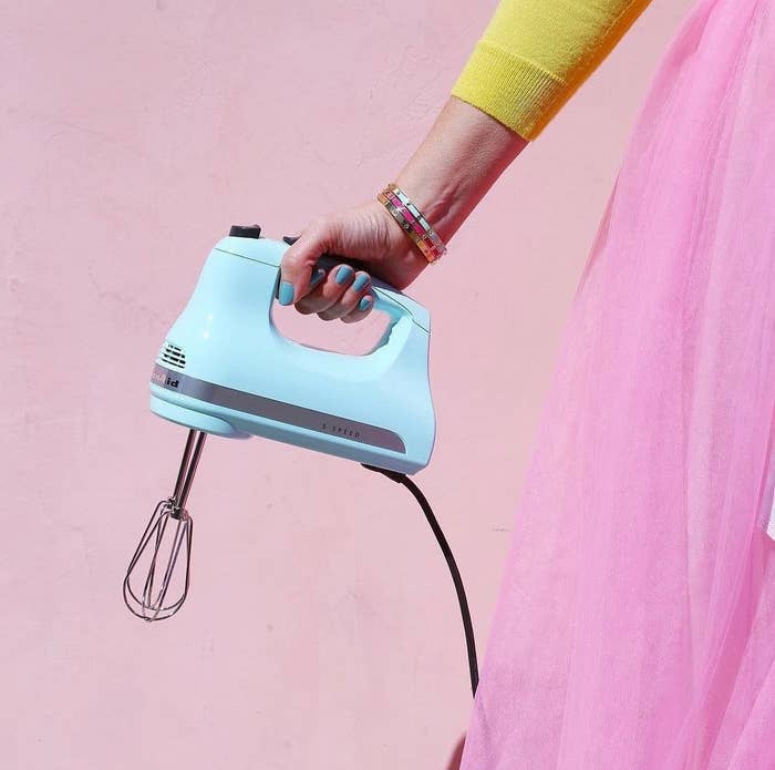 A person holding the hand mixer against a colourful backdrop