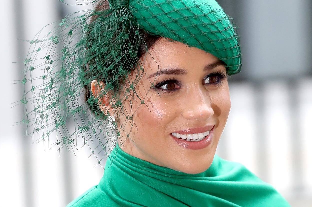 Meghan Markle is photographed smiling and wearing a green hat