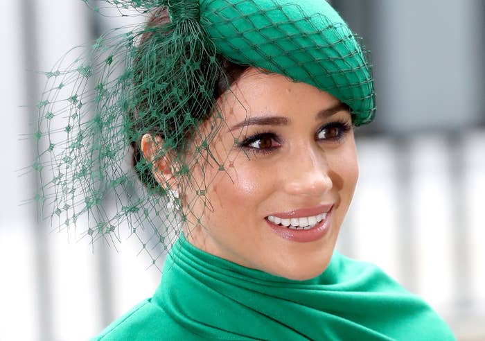 Meghan Markle is photographed smiling and wearing a green hat