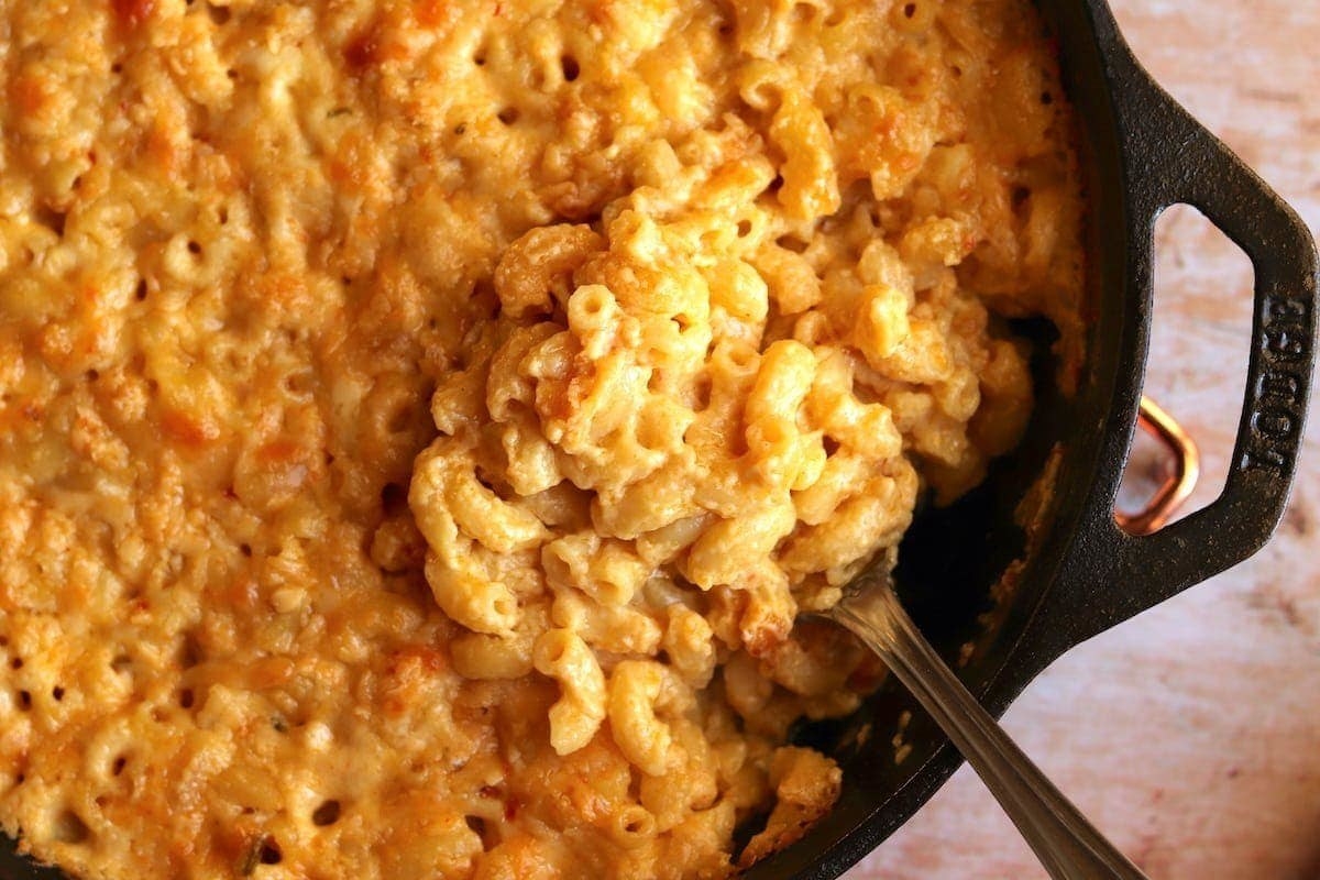 A large skillet of creamy mac &#x27;n&#x27; cheese with a spoon scooping some of it out.