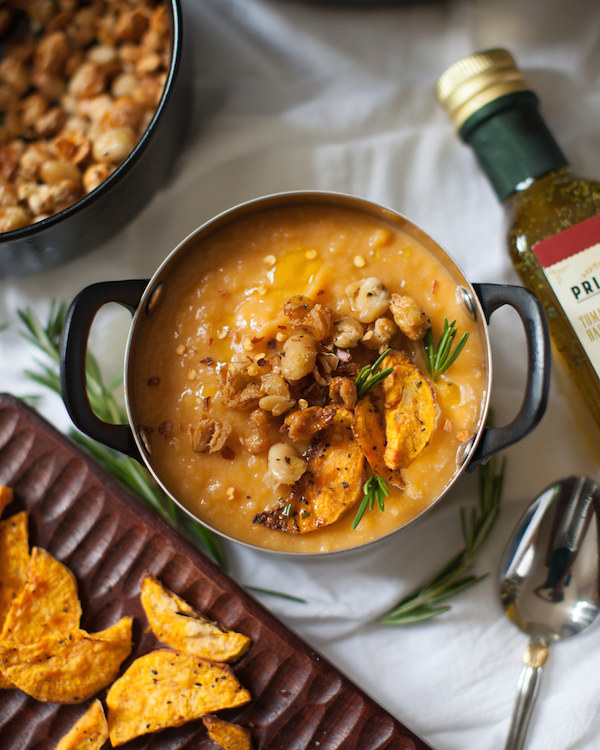 A pot filled almost to the top with sweet potato bisque topped with fried white beans and sweet potato slices.