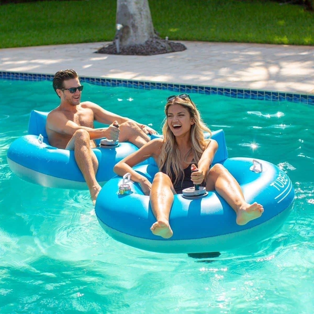 Two people racing each other while sitting in their pool floats. Each float has a controller in the center of the tube.
