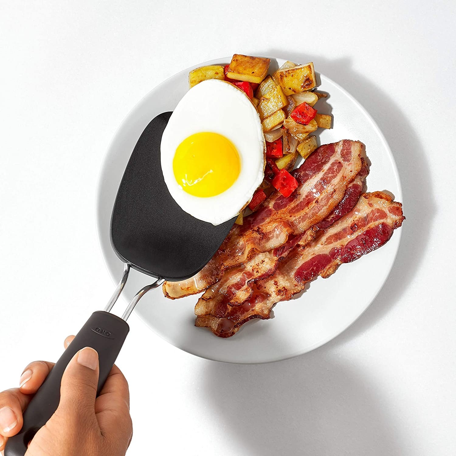 Someone using the flipper to slide a sunny-side up egg onto a plate full of breakfast food