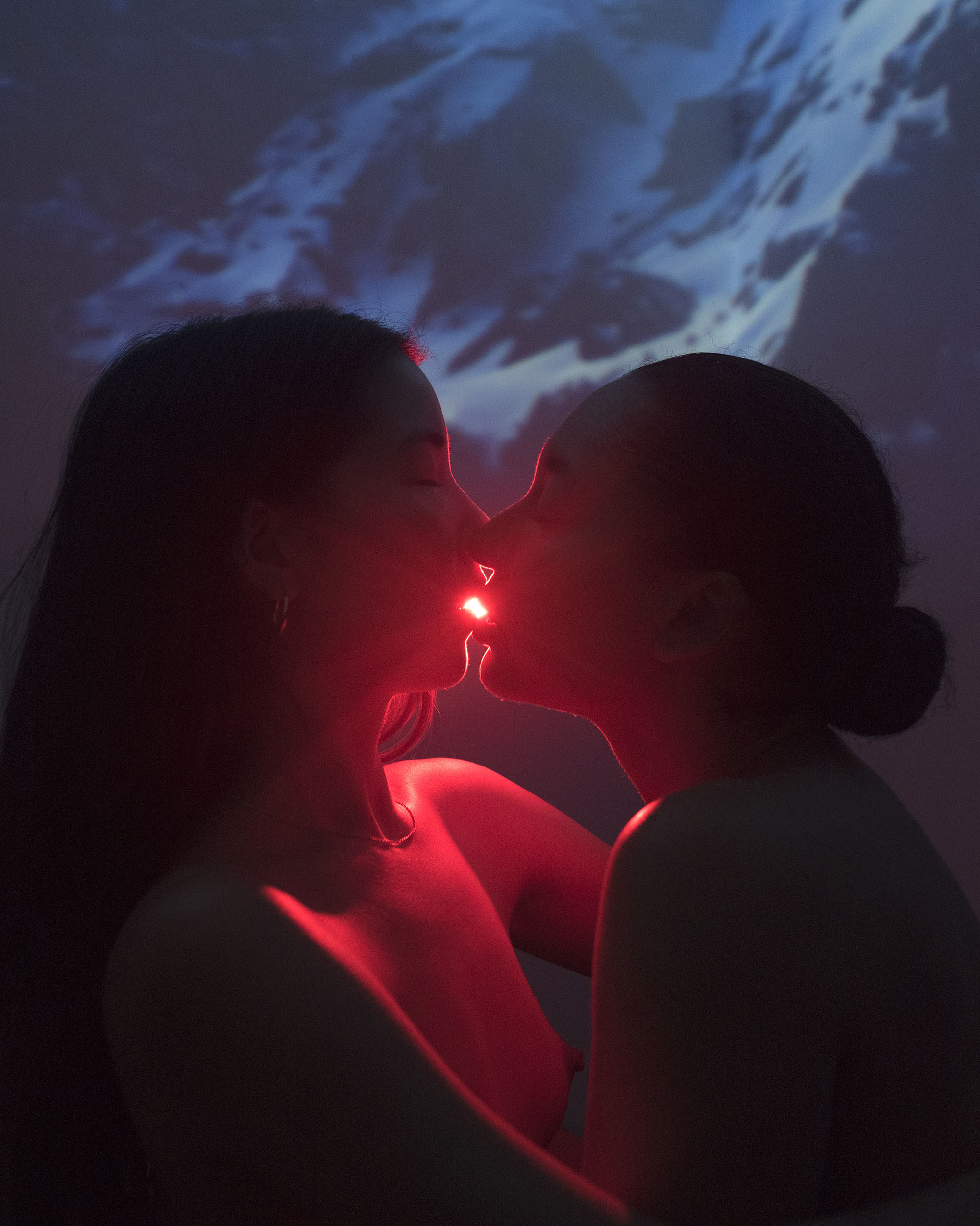 Two women kissing with a red light behind them 