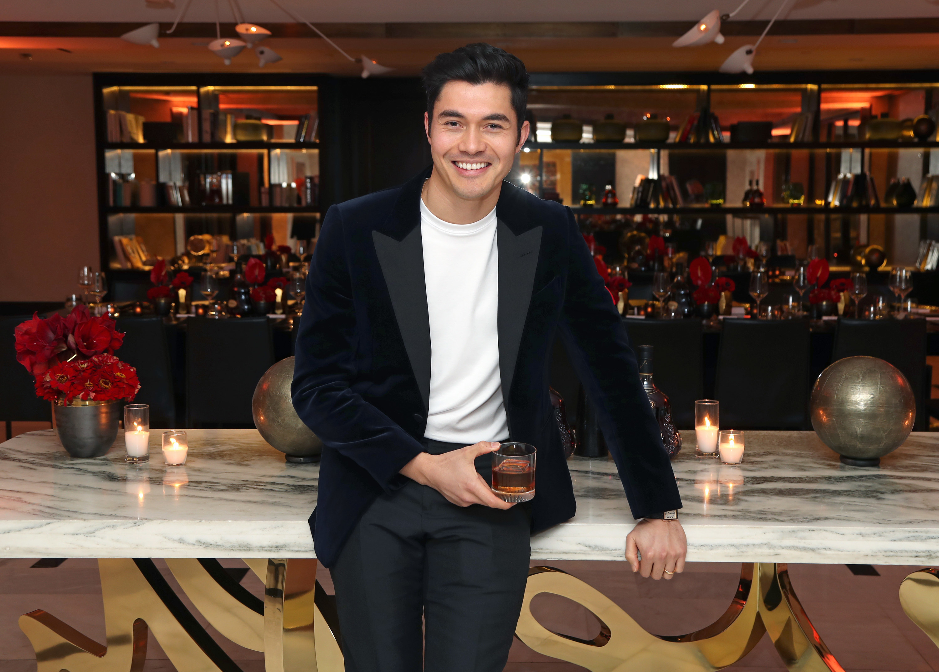 Henry Golding smiles while holding a glass of Hennessy