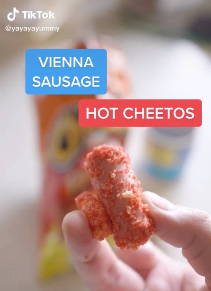 A person holding a vienna sausage and a hot Cheeto