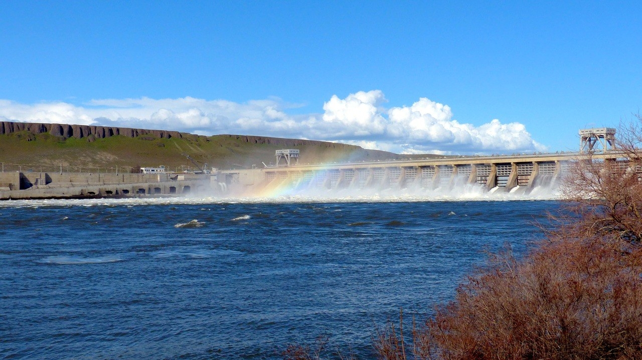 A rainbow appears over the river of a hydroelectric dam.
