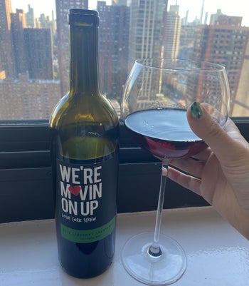 A BuzzFeed editor holding a glass of red wine next to a bottle 