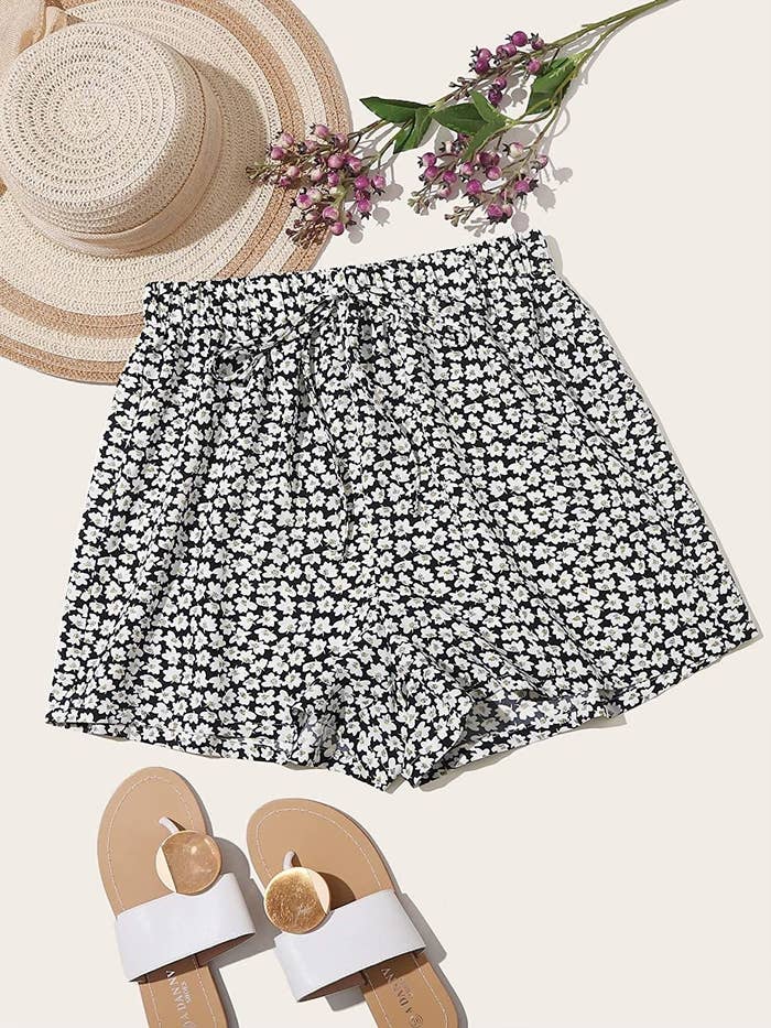 floral shorts next to a pair of sandals, a hat, and some flowers