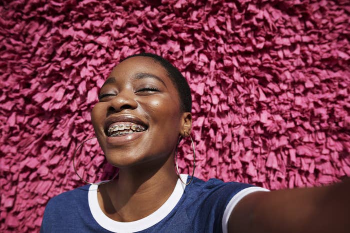 Portrait d’une personne souriante avec les yeux fermés appuyée contre un mur texturé