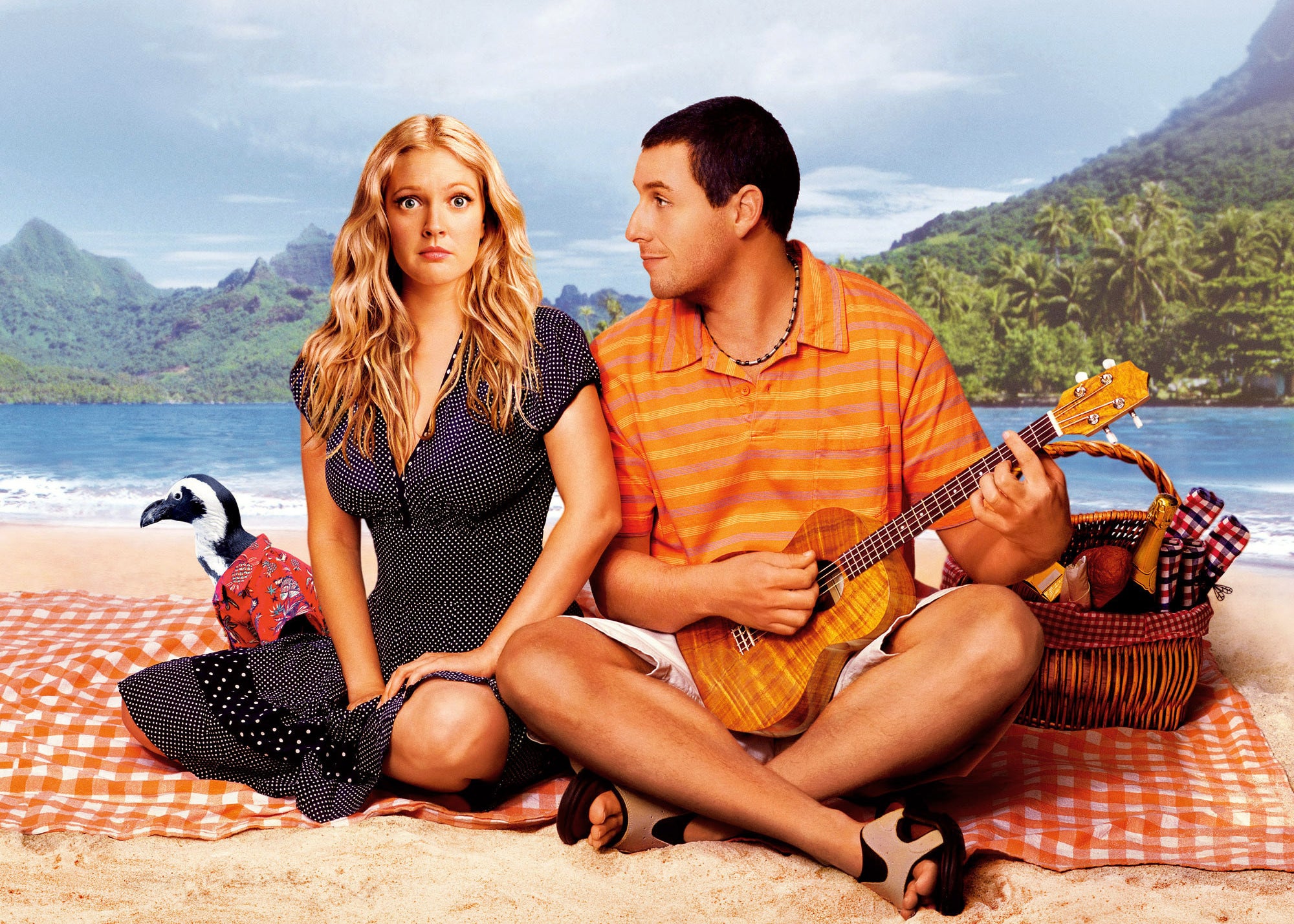Drew Barrymore and Adam Sandler sit on a blanket on the sand on a beach