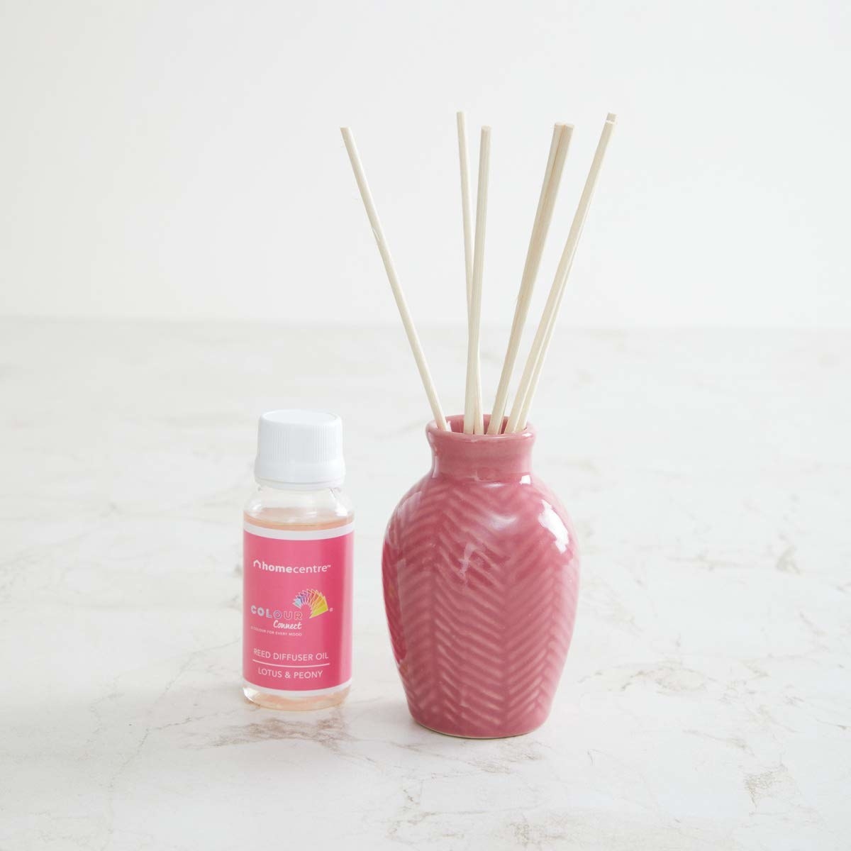 The reed sticks are placed in pink ceramic pot, and there&#x27;s a bottle of diffuser oil placed next to it.