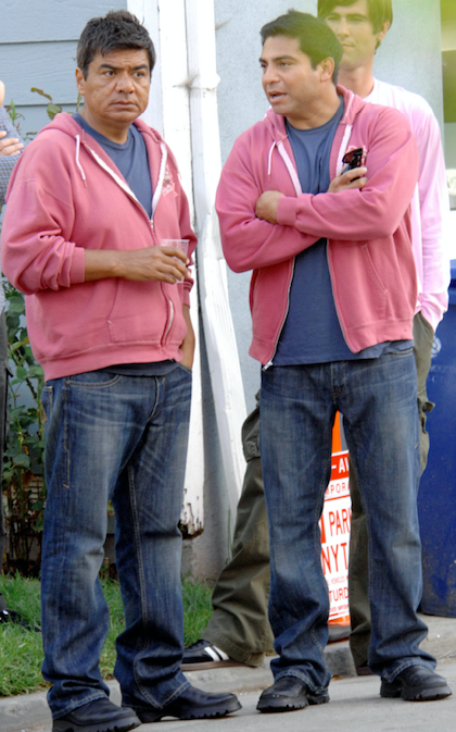 George Lopez wearing loafers, jeans, and a ratty hoody standing next to a man dressed in the exact same clothes