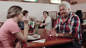 Gif of Guy Fieri sitting at a diner table and making a funny face