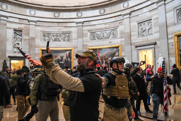 Several people wearing military-style fatigues and holding US flags are packed into the Capitol rotunda