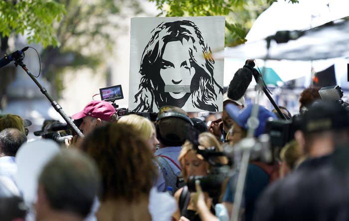 In a crowd, someone holds up a sign that depicts Britney Spears&#x27; face with duct tape covering her mouth