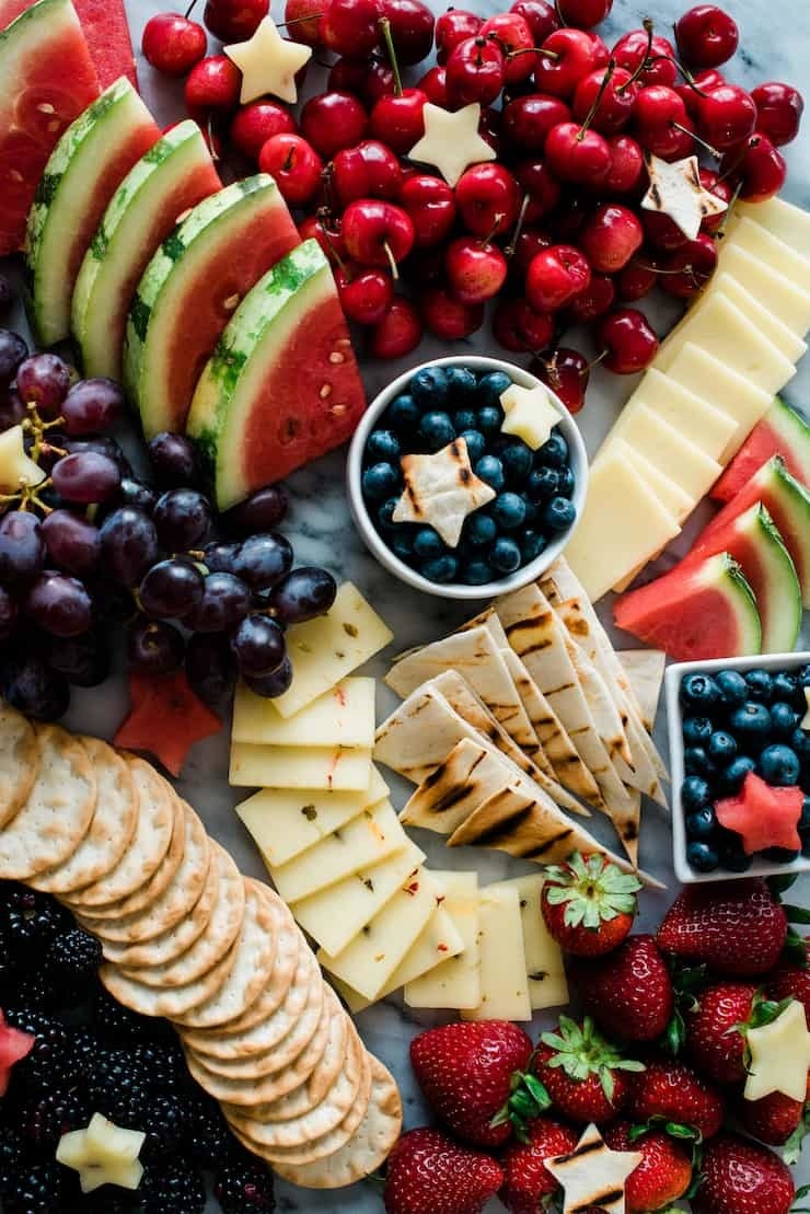 A cheeseboard garnished with blackberries, strawberries, blueberries, watermelon, grapes, pita, and crackers.