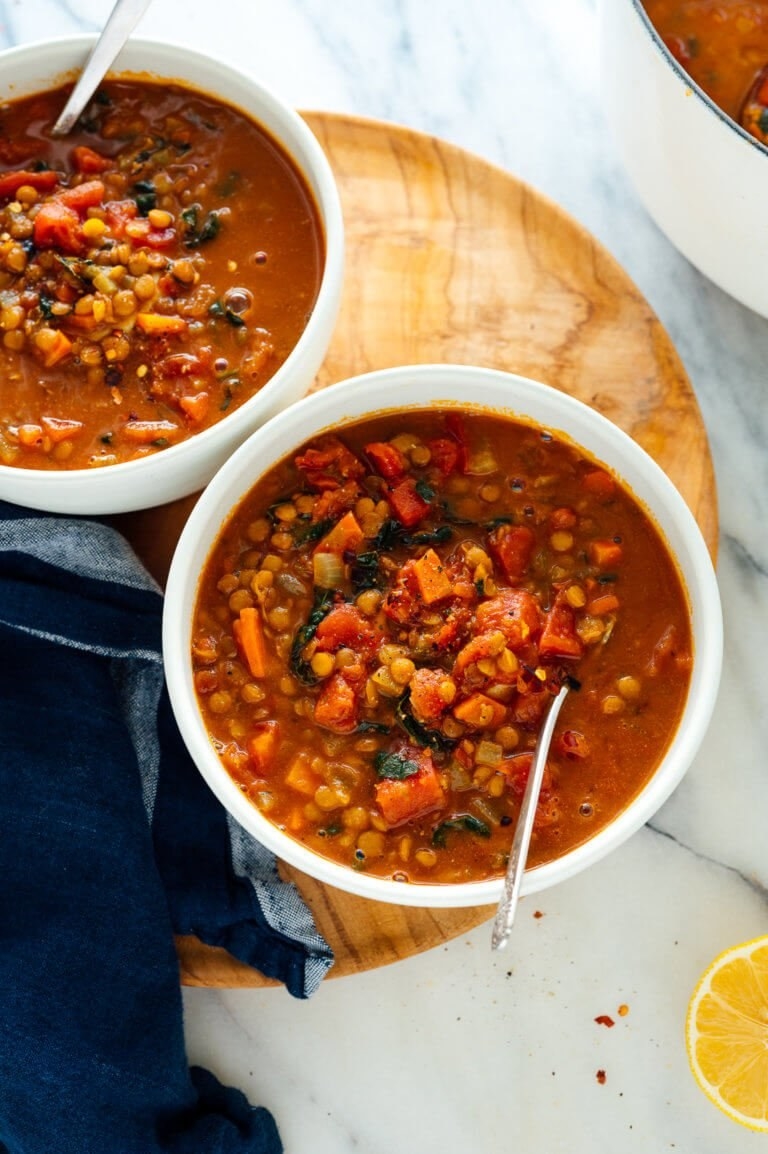 Two bowls of freshly made lentil soup placed on a circular wooden board.