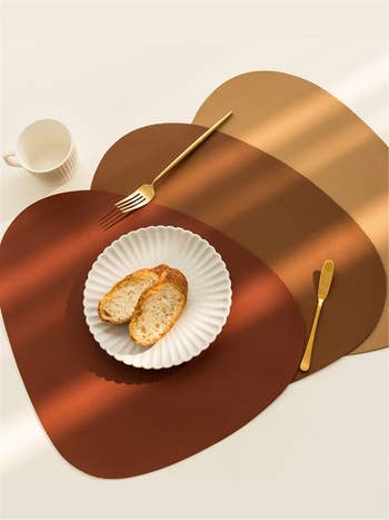 three rounded triangle placemats with a plate of bread and golden utensils on top 