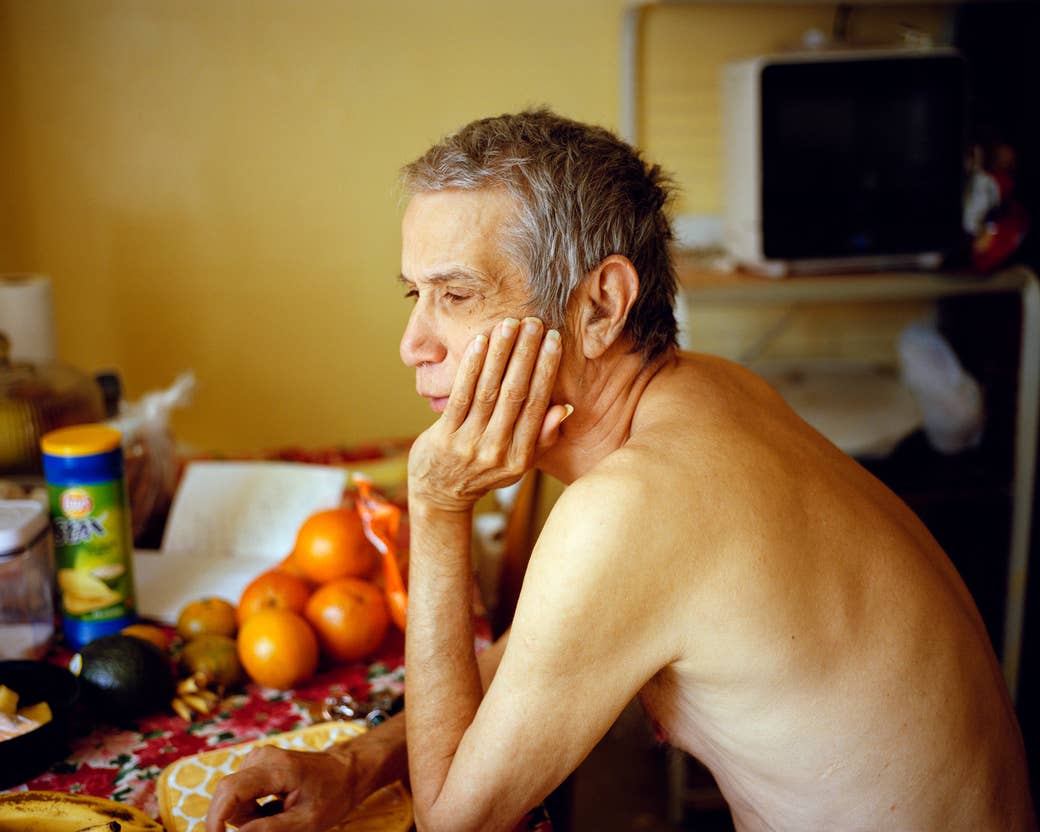 A man sitting shirtless at a table with oranges and potato chips on it