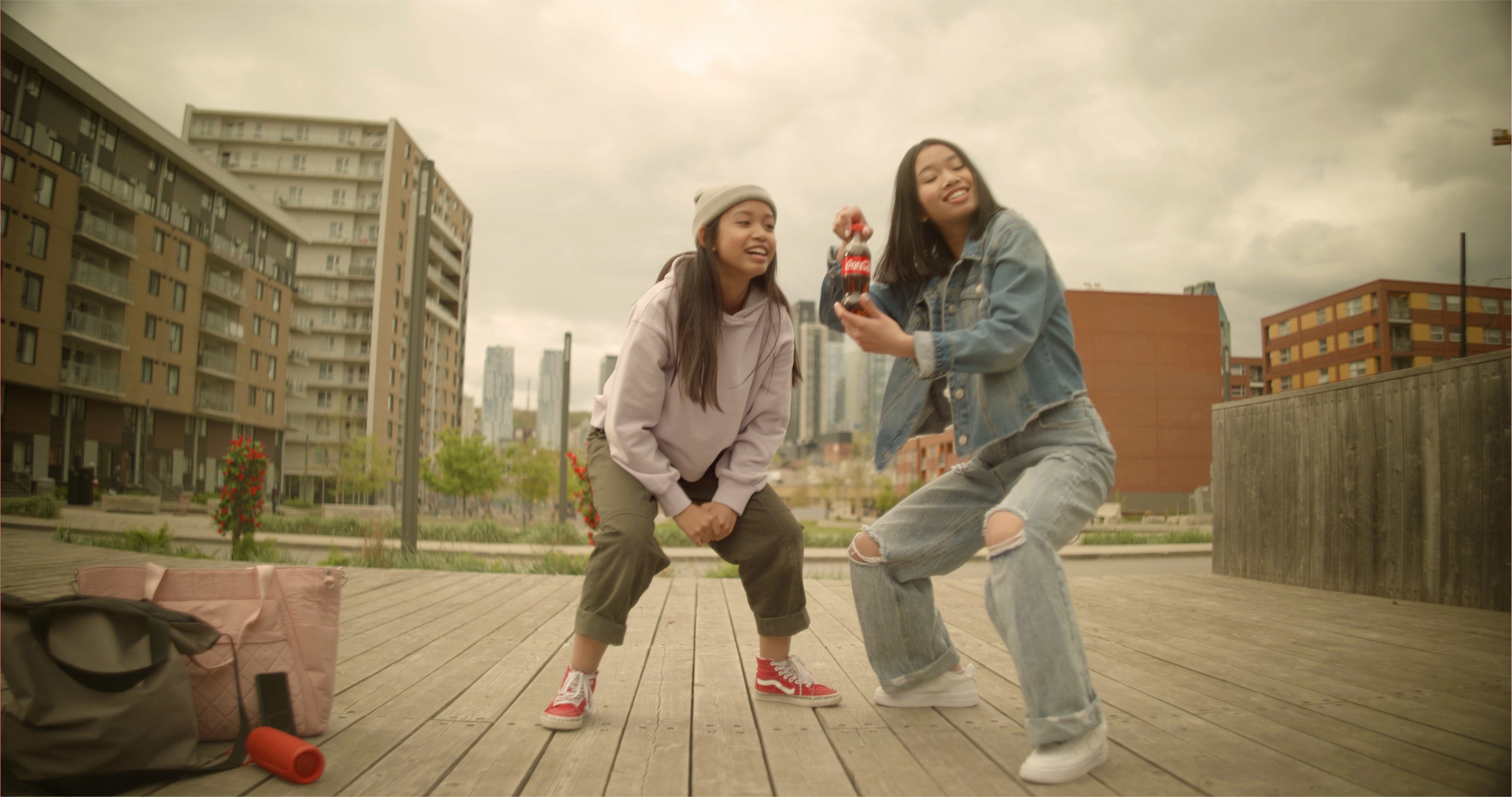 Two young people dancing on a boardwalk while holding Coca-Cola mini bottles