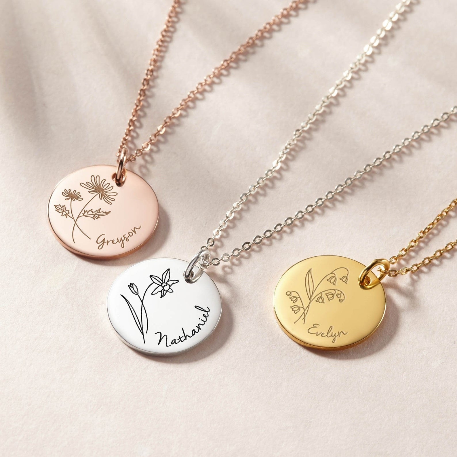 three necklaces with circular charms on them with flowers and a name etched into them