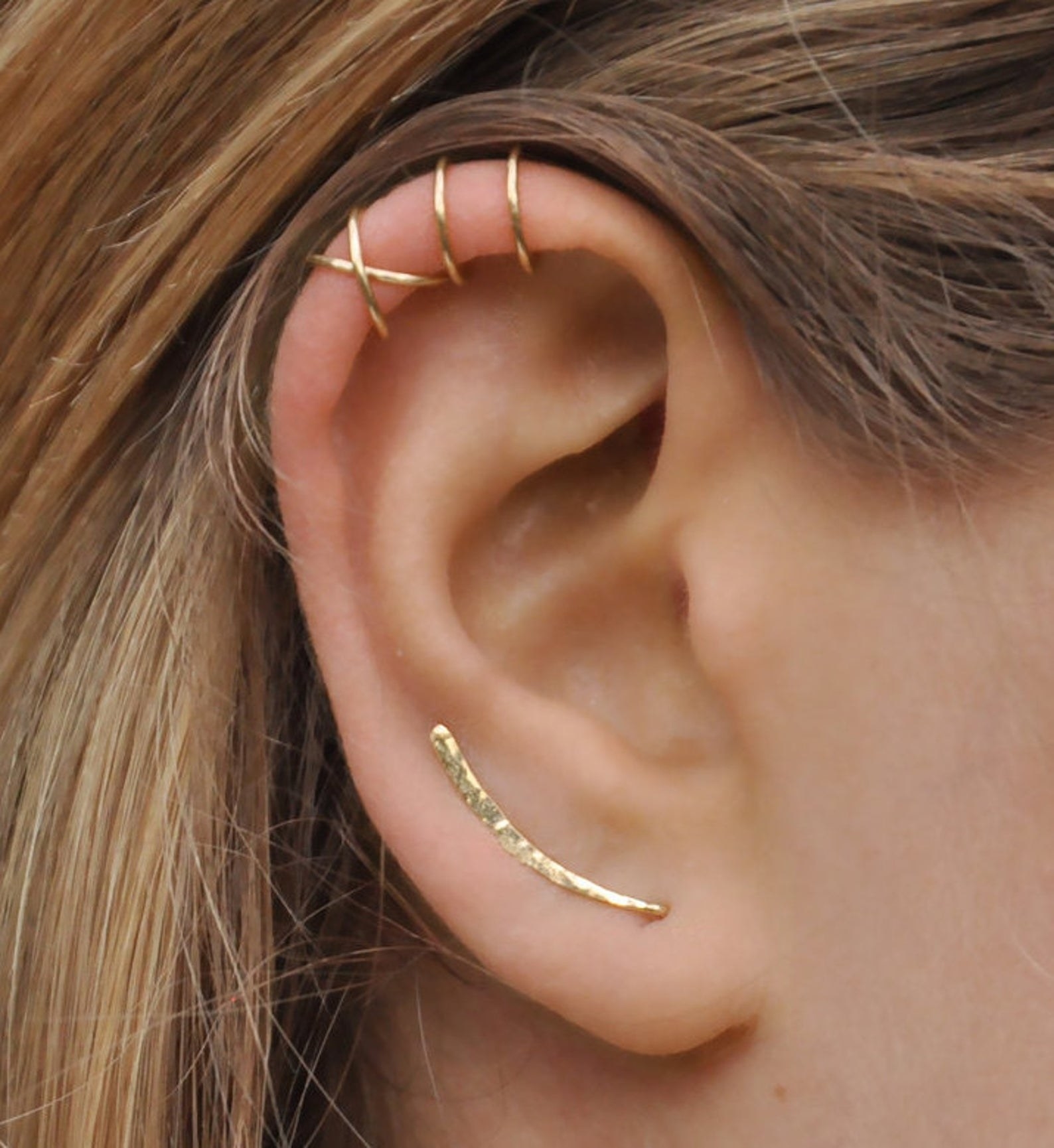 a gold ear crawler and two cuffs on the top of a model&#x27;s ear