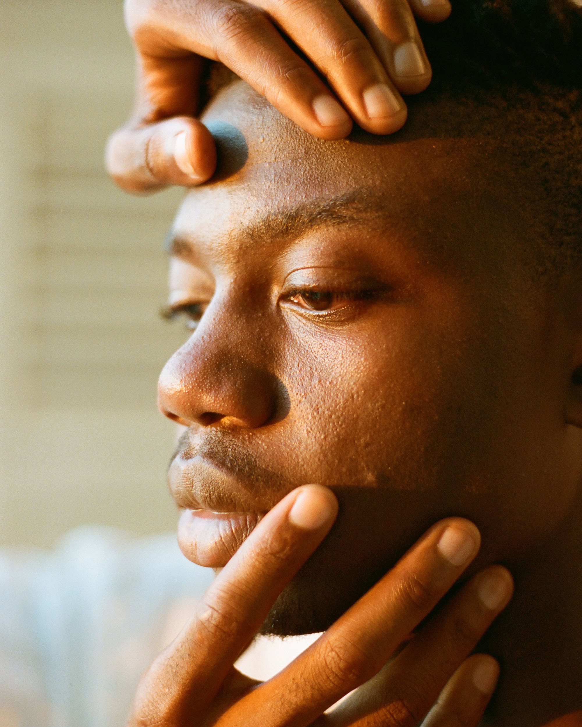 A young man looks away from the camera, hands cradle his face