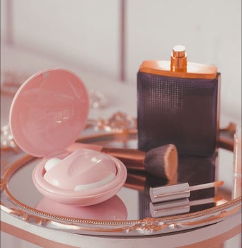 lifestyle image of the Diskreet Air in its pink carrying case on a circular mirror tray, surrounded by makeup brushes and perfume