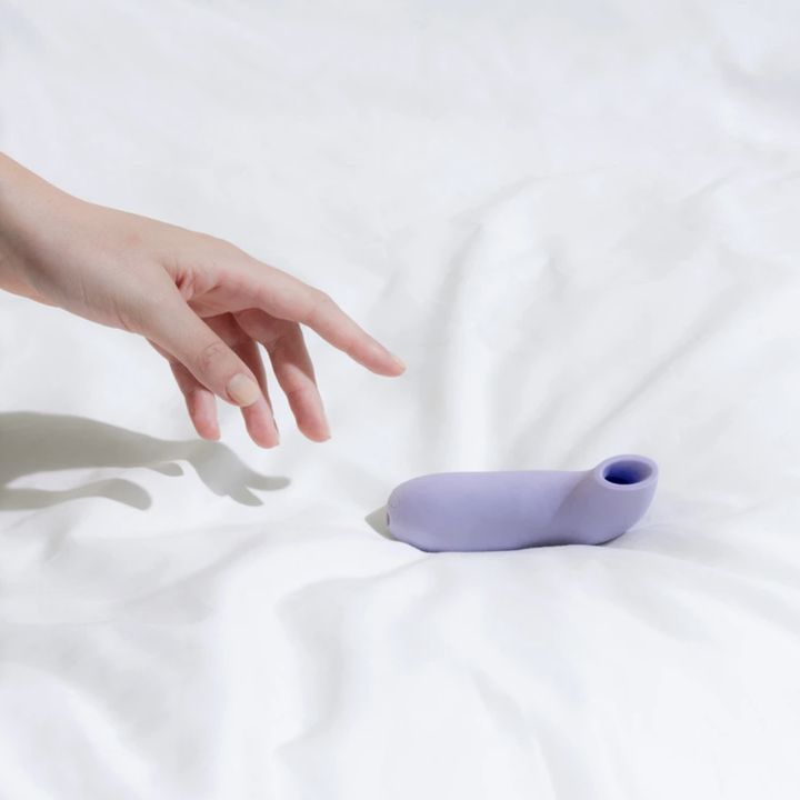 lifestyle image of the lavender-colored Aer on a white bedspread, hand reaching out for it