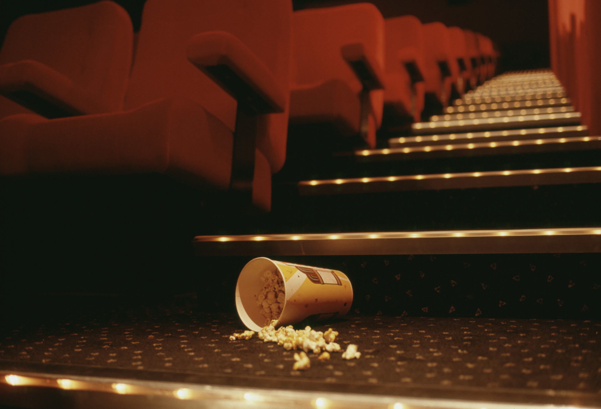 Spilled popcorn at the base of the lit stairs of a movie theater, looking up the aisle with seats on either side