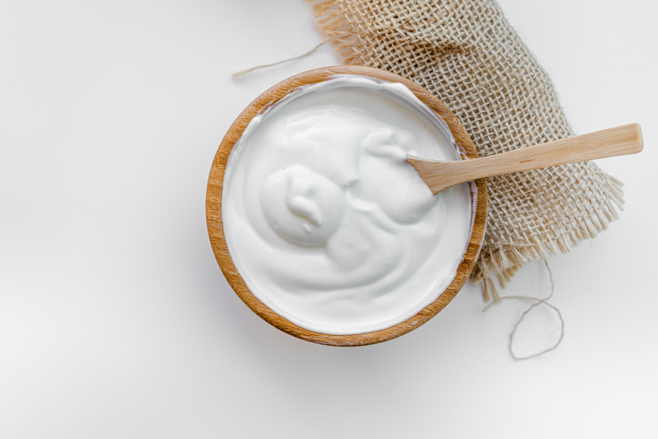 A wooden bowl of sour cream with a wooden spoon sticking out of it, and rolled up. burlap under one side