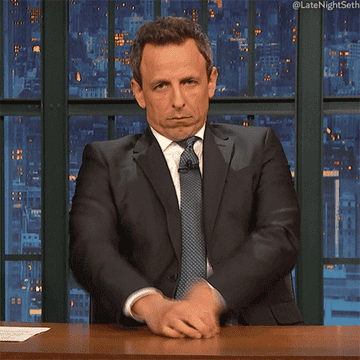 Seth Myers at his desk crossing his arms huffily with an unamused face