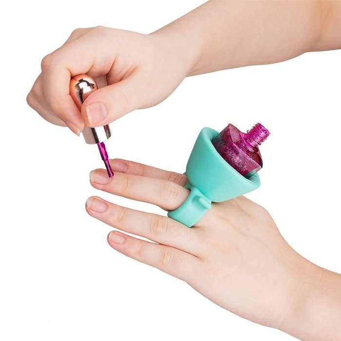 A person using the holder to securely hold a glittery pink nail polish bottle. It&#x27;s placed like a ring on their finger.