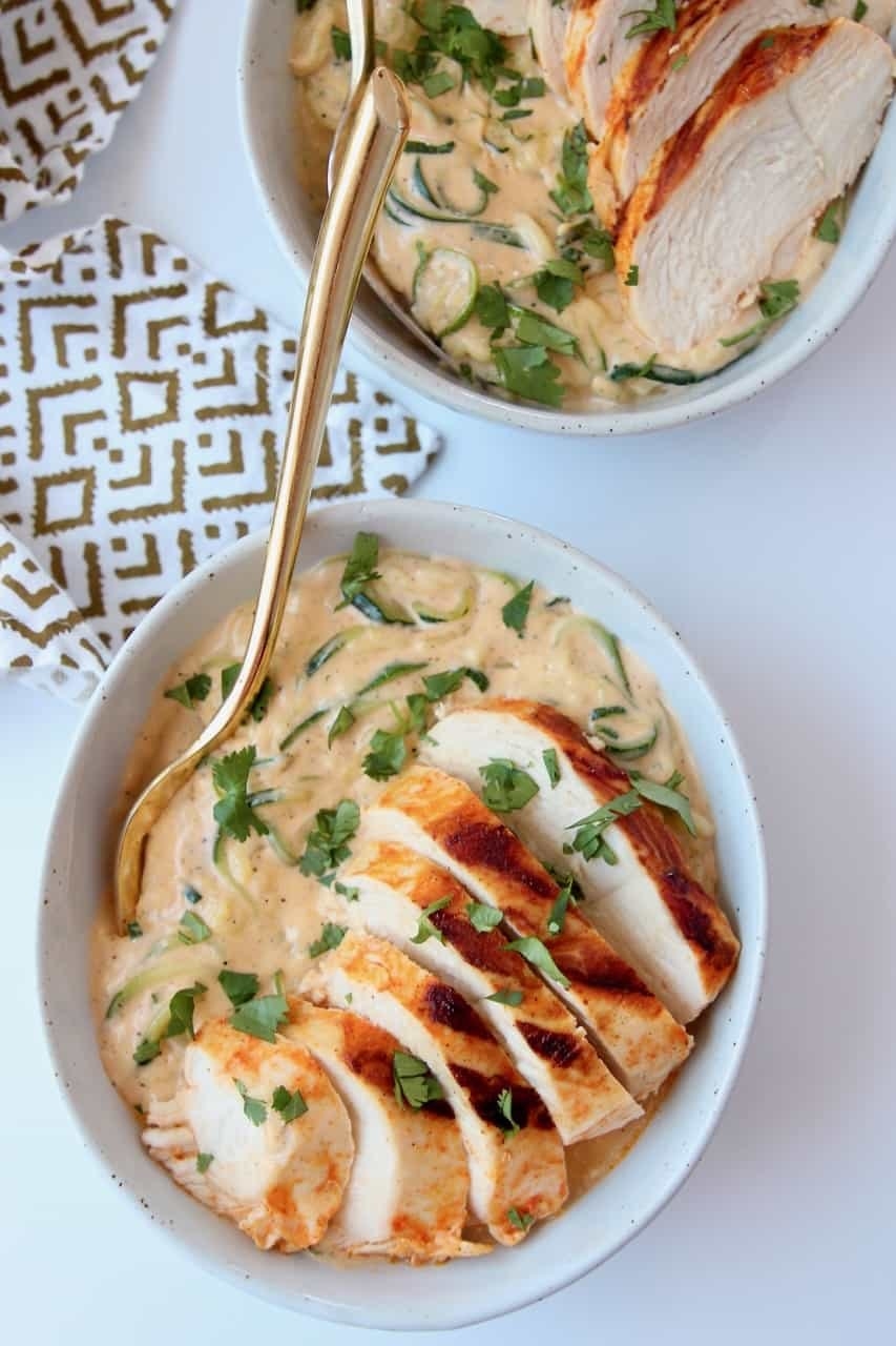 Creamy sauce and sliced chicken in a white bowl with a gold spoon