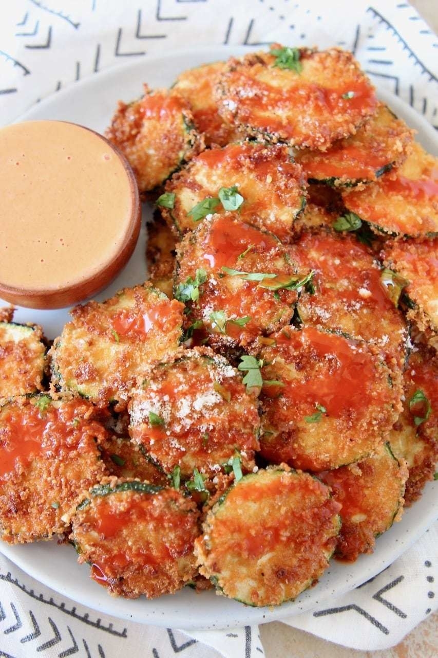 Fried zucchini slices coated in buffalo sauce on a white plate