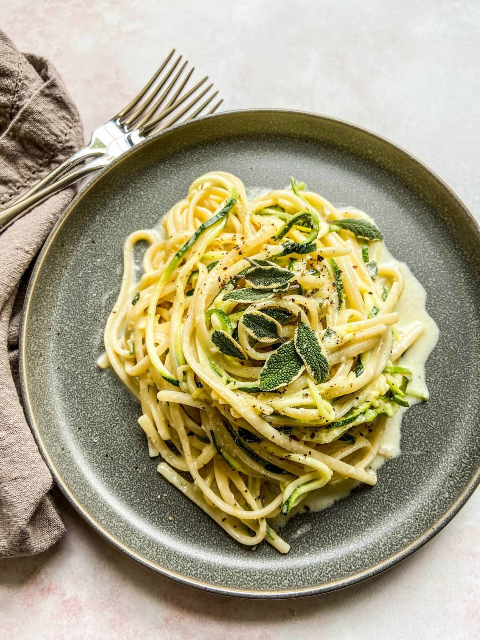 Zucchini noodles piled up on a grey plate topped with herbs